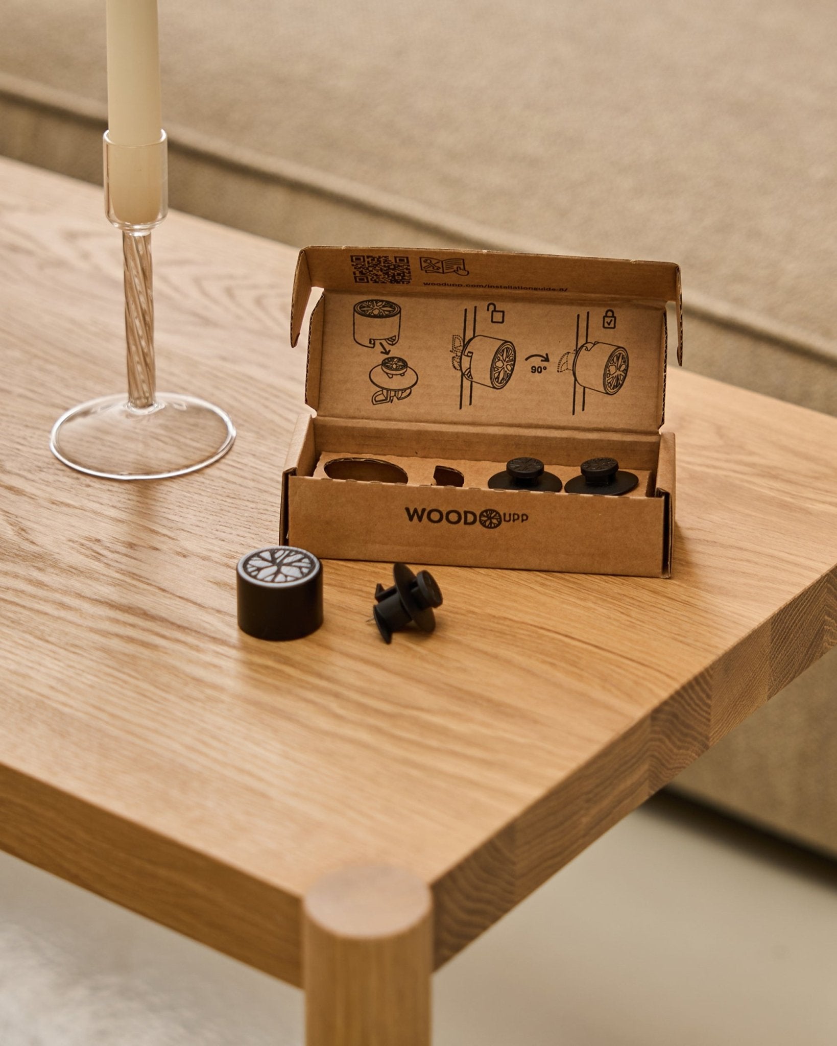 Dupps | Light (3 pcs + 1 tool) by WoodUpp—three black round accessories and one tool in an open box on a wooden table, candlestick and sofa behind.